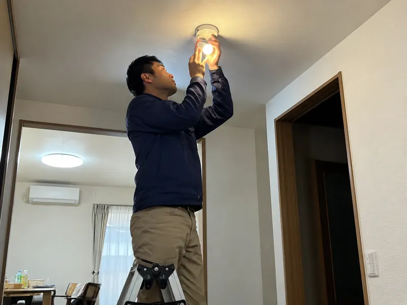脚立に乗って電球を交換するスタッフ
